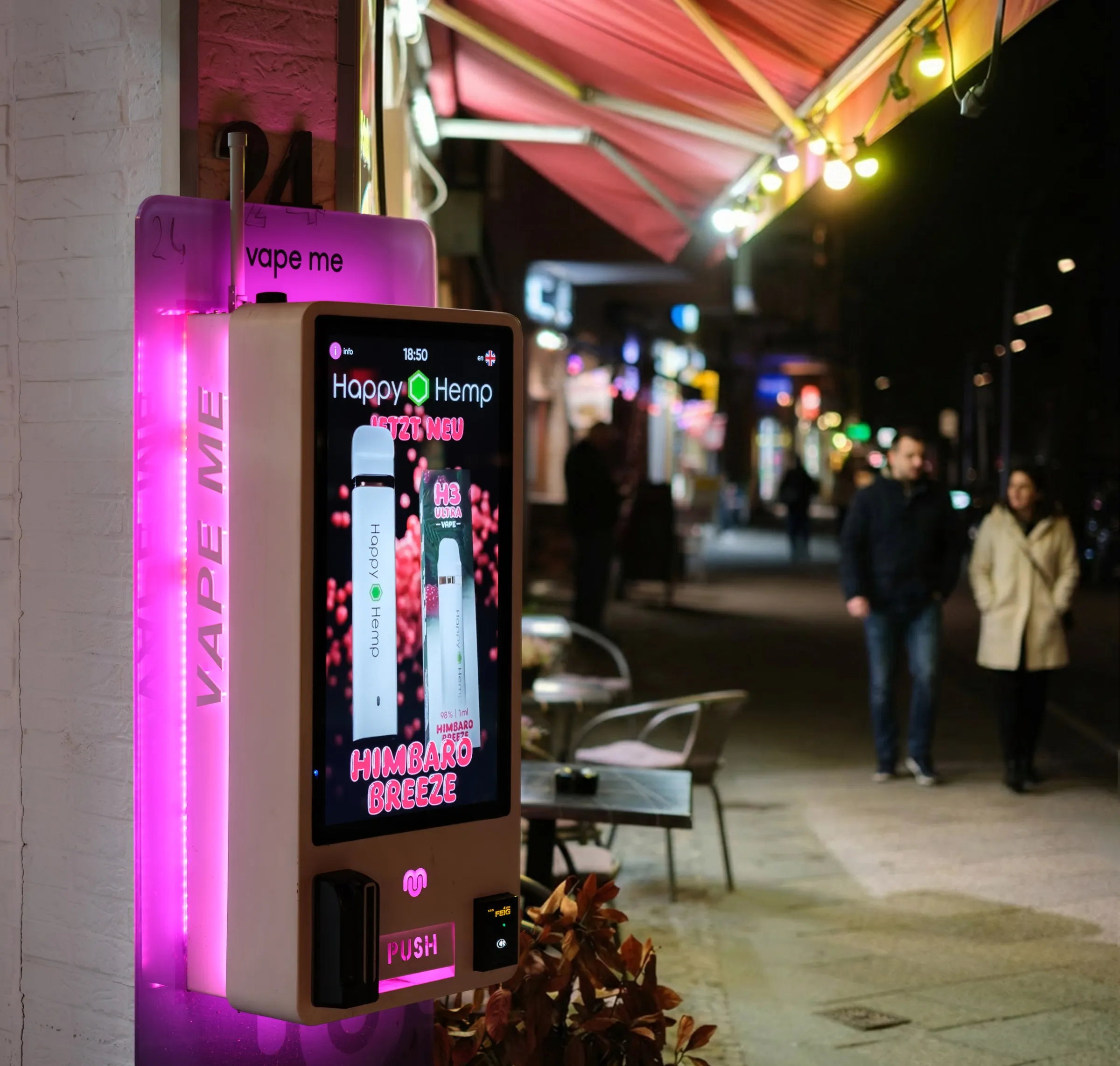 Vape4Me-Automat in einer urbanen Berliner Straße bei Nacht, im Hintergrund Passanten und Restaurant-Beleuchtung – Foto: Matthias Stoewer